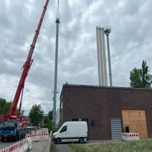 Ein blauer Hubwagen mit rotem Hydraulik-Arm richtet den neuen Schornstein für die Energiezentrale des Quartiers Maselake korrekt aus.