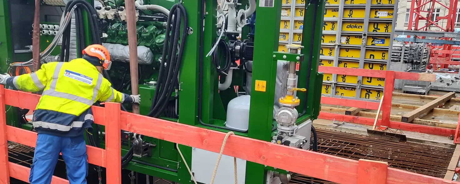 Ein Arbeiter weist den Kran an das Blockheizkraftwerk auf den Boden abzusetzen