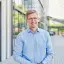 Gunnar Wilhelm, Managing Director der GASAG Solution Plus, steht mit blauem Hemd vor einem Gebäude und lächelt in die Kamera