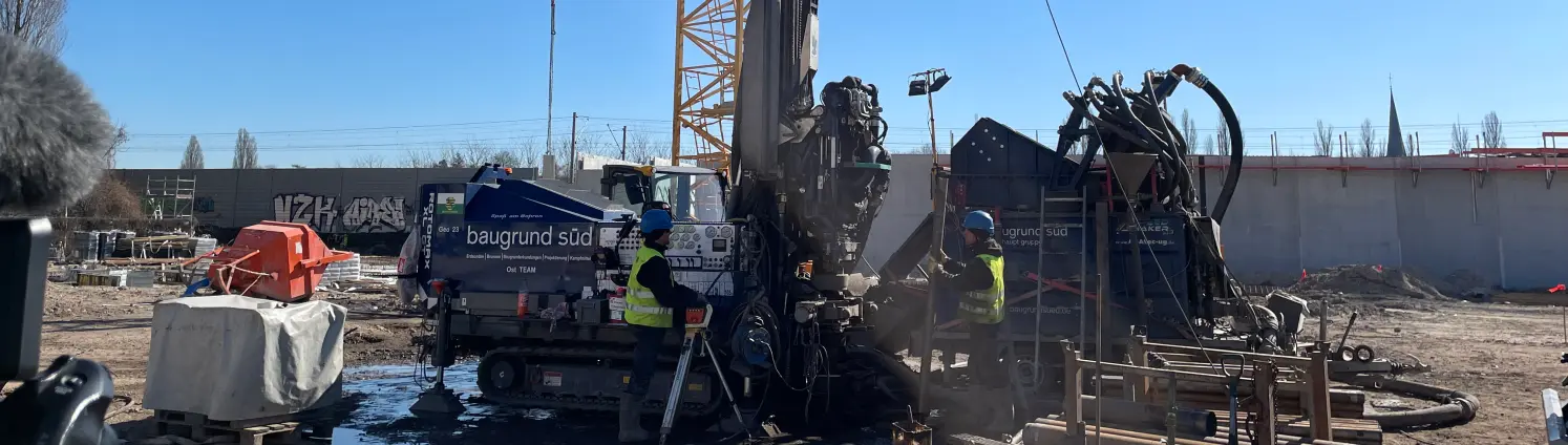 Auf einer Baustelle werden Geothermie-Bohrungen vorgenommen, zwei Bauarbeiter stehen neben dem Bohrer
