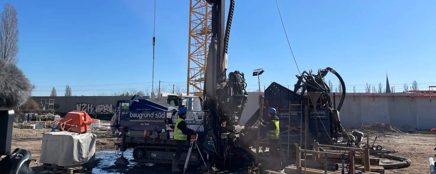 Auf einer Baustelle werden Geothermie-Bohrungen vorgenommen, zwei Bauarbeiter stehen neben dem Bohrer