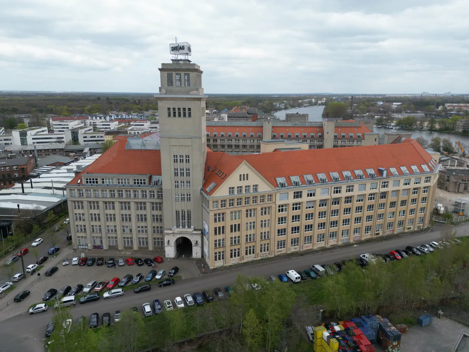 Luftaufnahme des denkmalgeschützten Peter-Behrens-Baus mit zentralem Turm, Innenhof und angrenzender Spree. Bild mit KI erstellt.