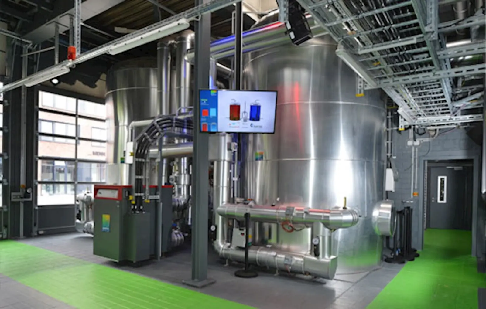 Energiezentrale mit großen Wärmespeichern, Rohrleitungen und digitaler Anlagensteuerung zur Wärmeversorgung von Gebäuden. Bild mit KI erstellt.