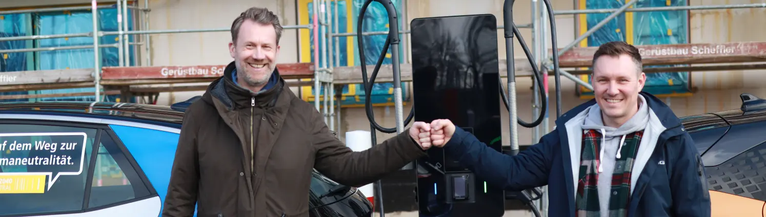 Zwei Männer stehen vor einer Ladesäule, an der gerade zwei E-Autos laden