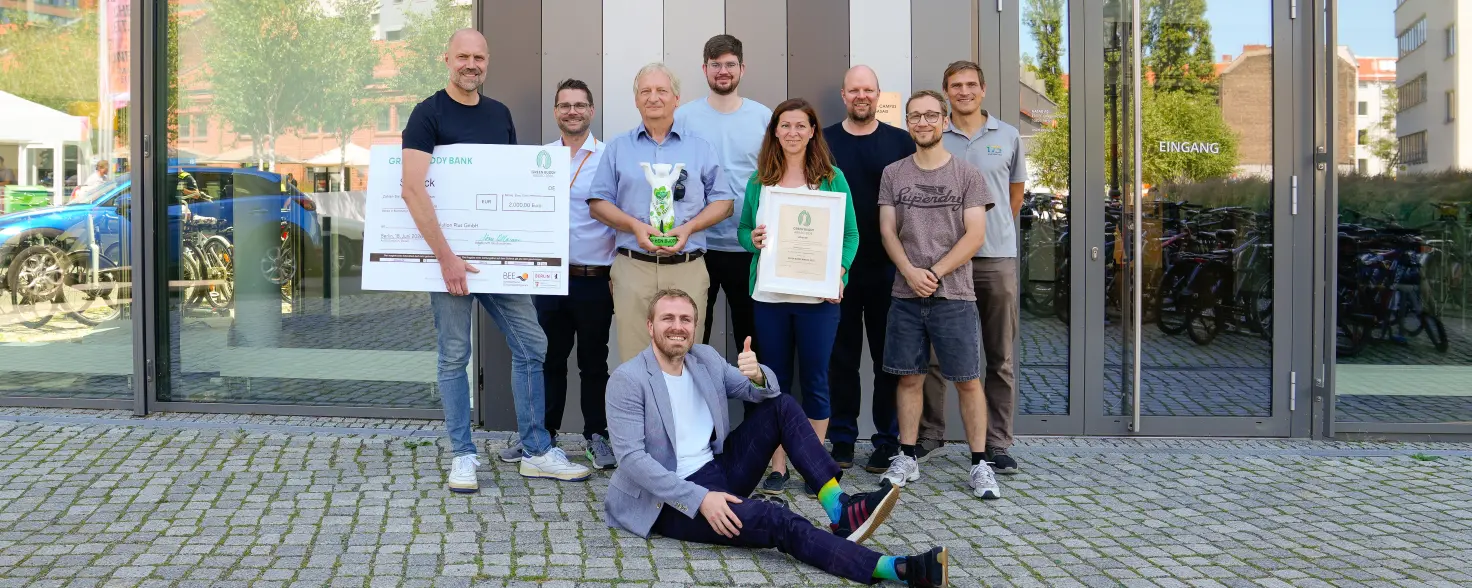 Acht Personen stehen vor dem Haupteingang des GASAG-Gebäudes zu einem Gruppenbild versammelt. Eine weitere Person sitzt vor der Gruppe auf dem Boden. Dieses Bild wurde vollständig mit KI erstellt.