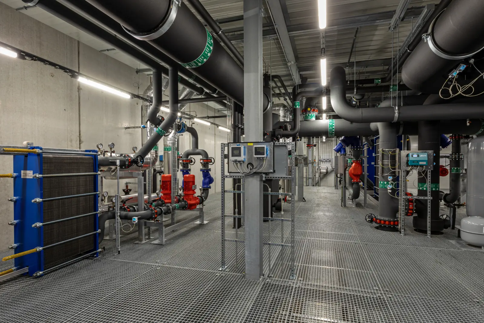 Technikraum mit Wärmetauschern, Pumpen, Rohrleitungen und Mess- sowie Steuerungstechnik in einer Energiezentrale. Bild mit KI erstellt.