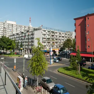 Ansicht des Pallasseums mit mehrgeschossigem Wohngebäude, zahlreichen Balkonen und Geschäften im Erdgeschoss an einer Kreuzung in Berlin. Bild mit KI erstellt.