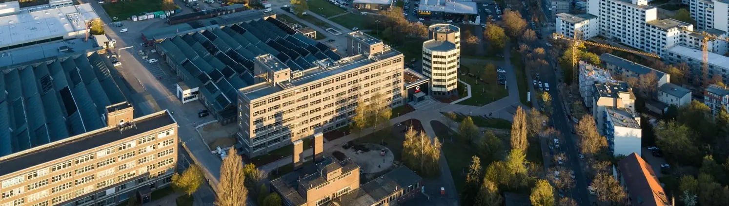 Projekt Ringberlin: Luftaufnahme eines Berliner Stadtteils mit Gewerbegebäuden, Straßen und Wohnblöcken im Abendlicht.