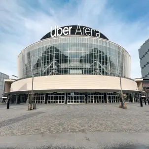 Uber Arena in Berlin mit markanter Glasfassade und großem beleuchtetem Schriftzug über dem Haupteingang. Bild mit KI erstellt.