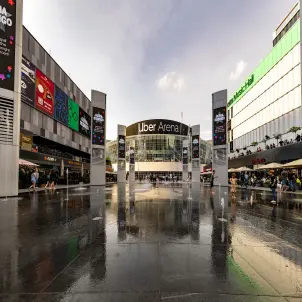 Uber Platz in Berlin mit Blick auf die Uber Arena, Wasserfontänen und spielenden Kindern zwischen Gastronomie- und Veranstaltungsgebäuden.