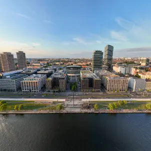 Luftaufnahme des Uber Platzes in Berlin mit der Uber Arena, modernen Büro- und Hotelgebäuden sowie der Spree im Vordergrund.