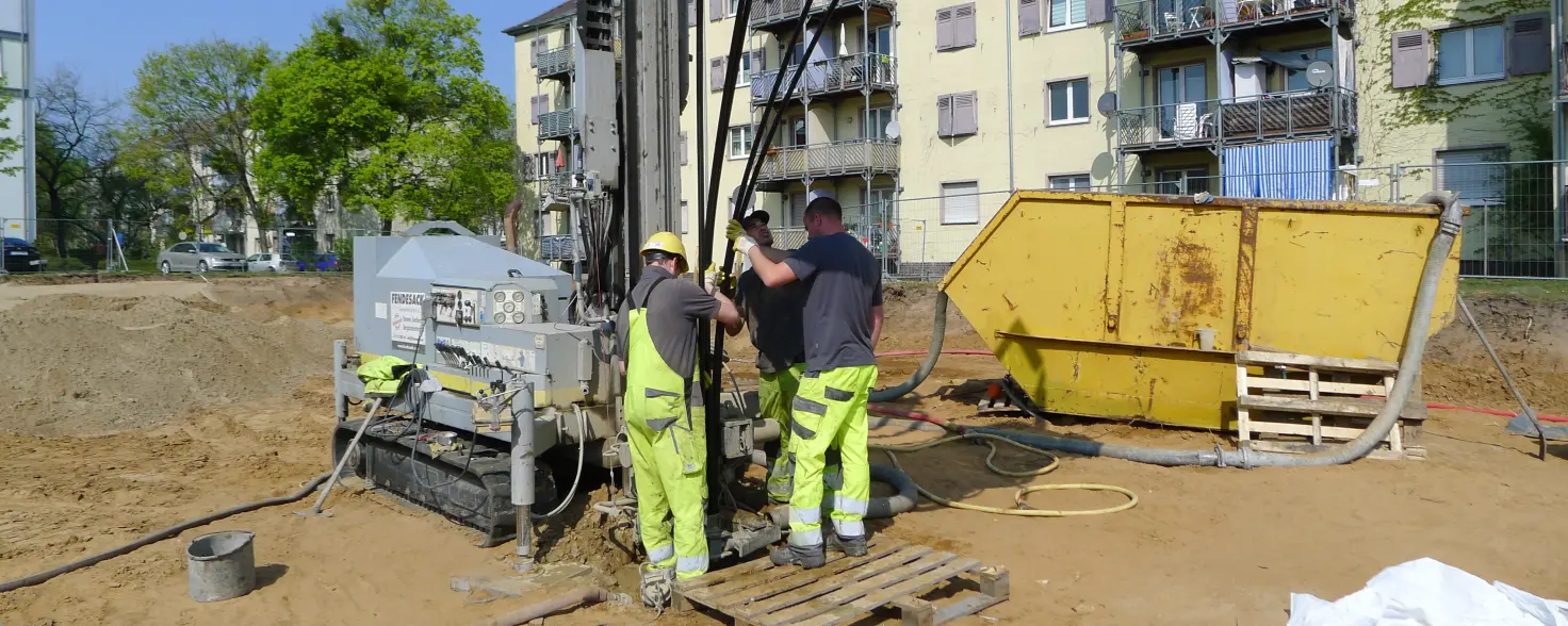 Drei Personen stehen auf einer Baustelle mit einer Maschine für eine Geothermie-Bohrung
